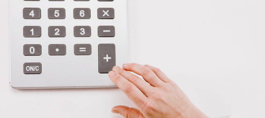 A hand pressing the plus button on a large calculator with oversized black and white buttons against a white background.