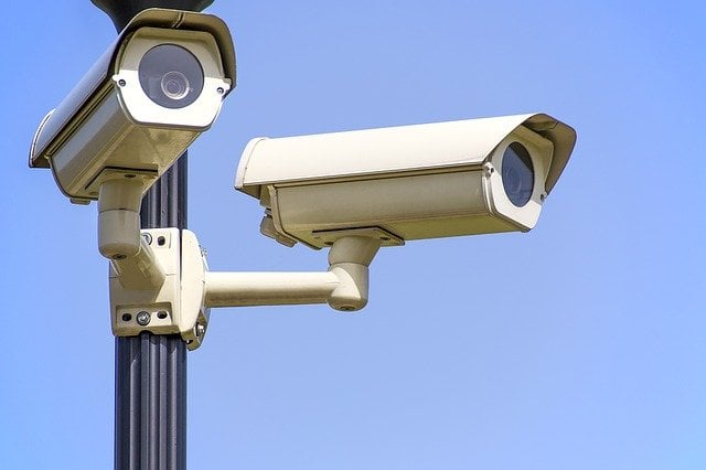 Two security cameras on a pole aimed in different directions.