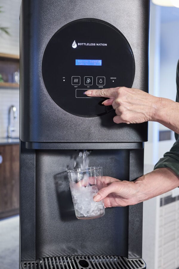 A person uses a water and ice dispenser, pressing the “Ice” button while holding a clear cup under the machine as ice dispenses into the cup.