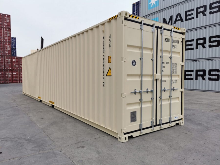A beige shipping container with closed double doors stands on a concrete surface in a shipping yard, surrounded by stacked containers labeled with the Maersk logo.