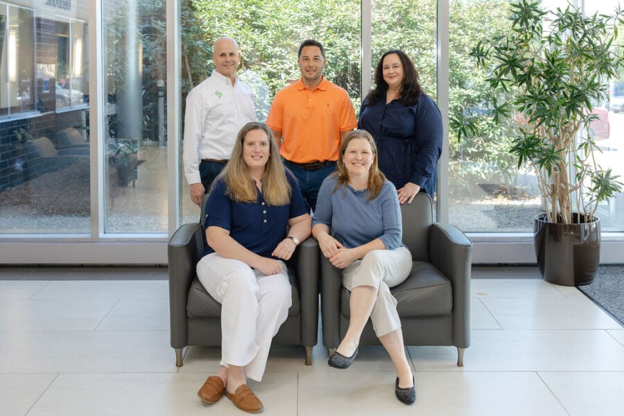 Three men and two women stand and sit together in a bright office lobby.
